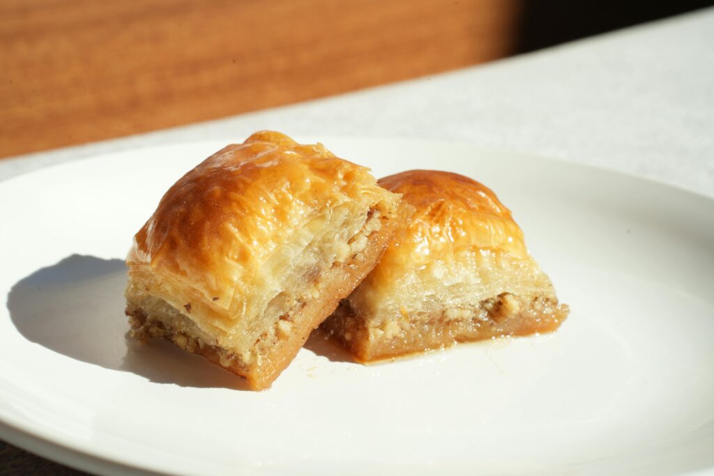 Close-up of two pieces of baklava on a white plate in bright lighting.